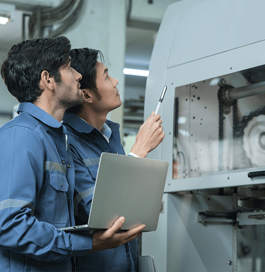 Two engineers inspecting machinery with a laptop on the factory floor